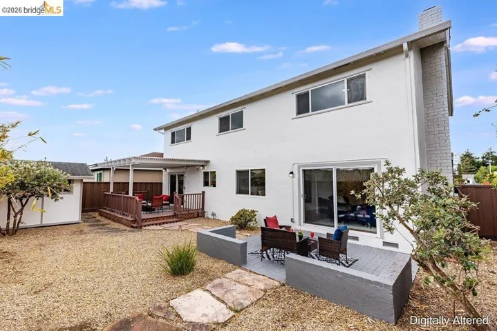 Expansive backyard featuring a gravel surface, a multi-level wood-deck patio with pergola, a separate paved patio area with low walls, a storage shed, and a stucco exterior with a brick chimney