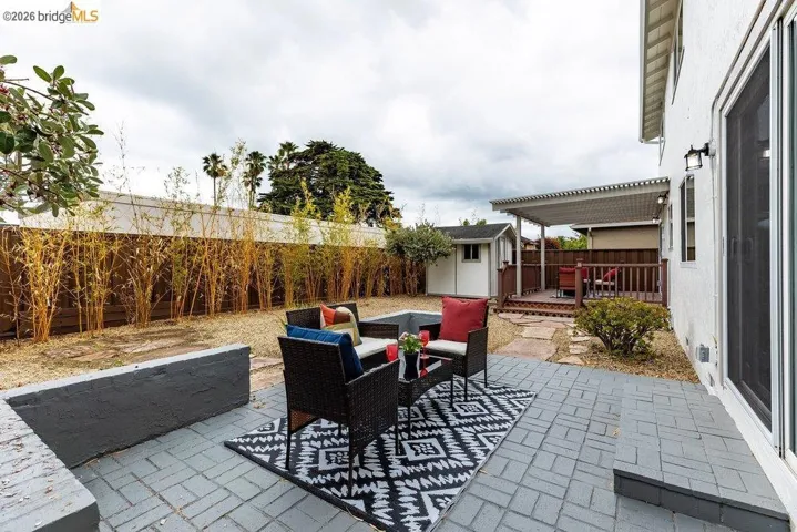 Expansive backyard featuring a gray paver patio, a raised wood deck with a slatted pergola, and a detached storage shed