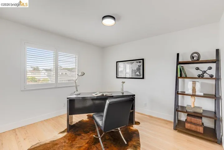 Wood-finish flooring with white baseboards, a window featuring white plantation shutters, and a ceiling-mounted light fixture
