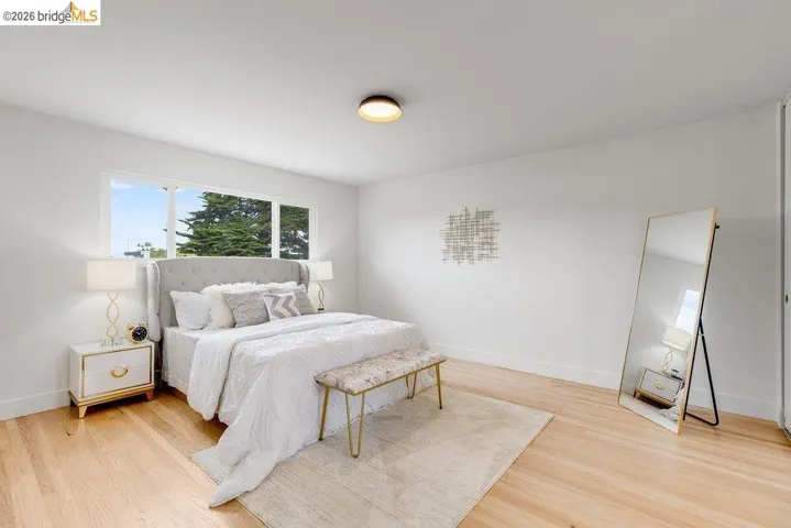 Bright bedroom featuring expansive windows, light wood-finish flooring, a contemporary flush-mount ceiling light, and white painted walls