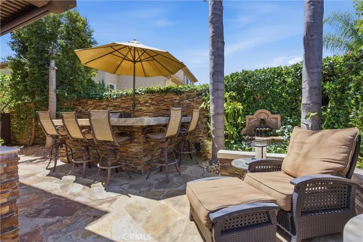 Private outdoor retreat with elevated bar seating, a built-in BBQ, lush tropical landscaping, and tranquil fountain accents