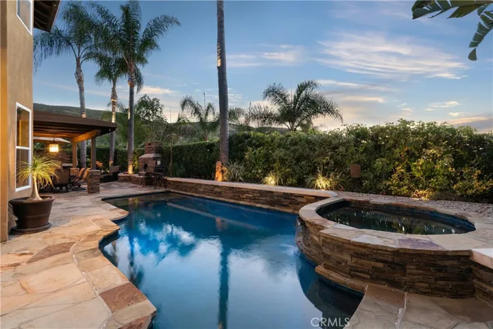 Resort-style backyard featuring a custom pool and spa, mature landscaping, and multiple areas for outdoor relaxation