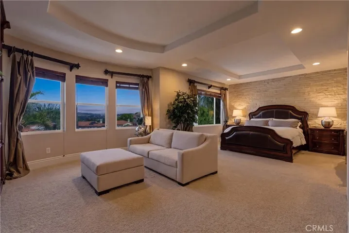 Image has been digitally edited. Spacious primary suite with a private sitting area, abundant natural light, and picturesque hillside and neighborhood views
