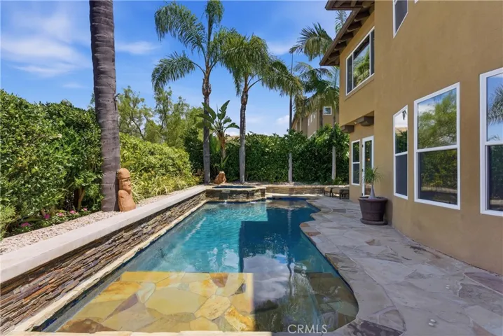 Resort-style backyard featuring a custom pool and spa, mature landscaping, and multiple areas for outdoor relaxation