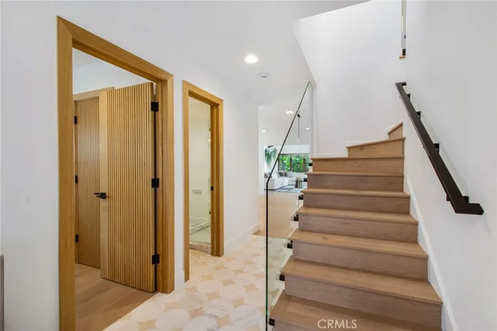 New white oak and glass staircase rises to the second level. Doors leading to 1st floor bed and bath | 305 Robinhood Ln., Eastside Costa Mesa 92627