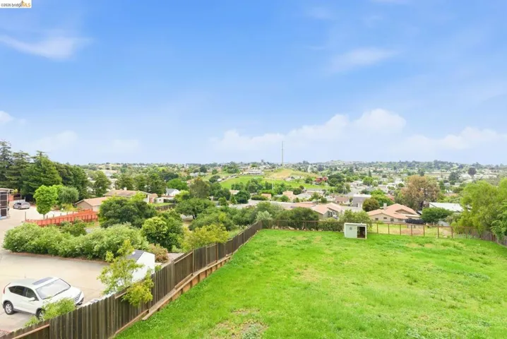 Expansive grassy yard area featuring a wood fence, storage shed, and distant neighborhood landscape