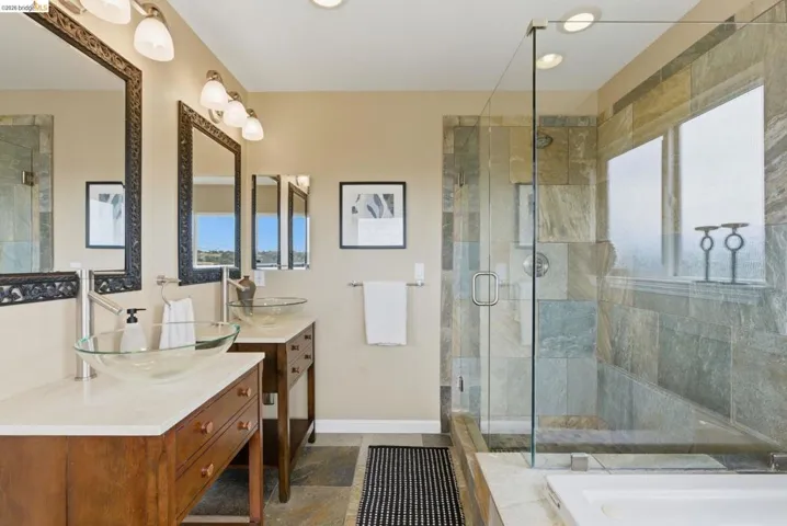 Bathroom featuring dual wood-finish vanity cabinets with stone countertops and glass vessel sinks