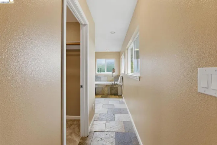 Hallway featuring large format stone tile flooring and multiple windows