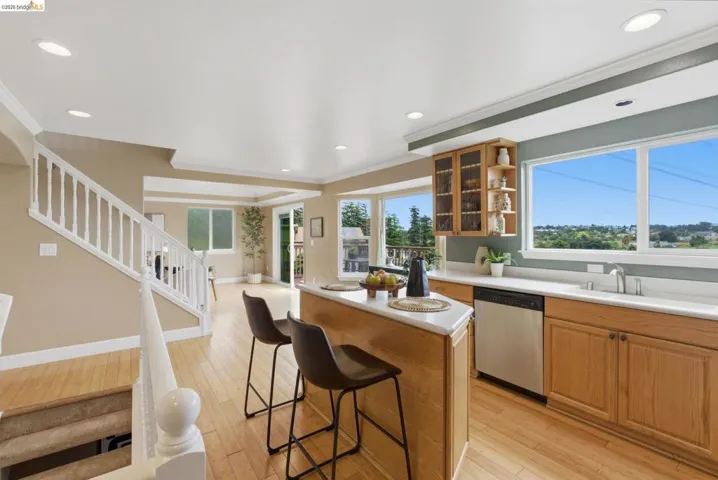 Open-concept kitchen with light wood-finish cabinetry, stainless steel dishwasher, white countertop, and expansive windows