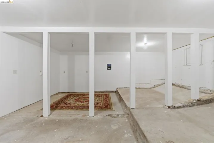 Unfinished lower level featuring exposed concrete flooring, white-painted support columns, recessed ceiling lighting, and a visible electrical panel