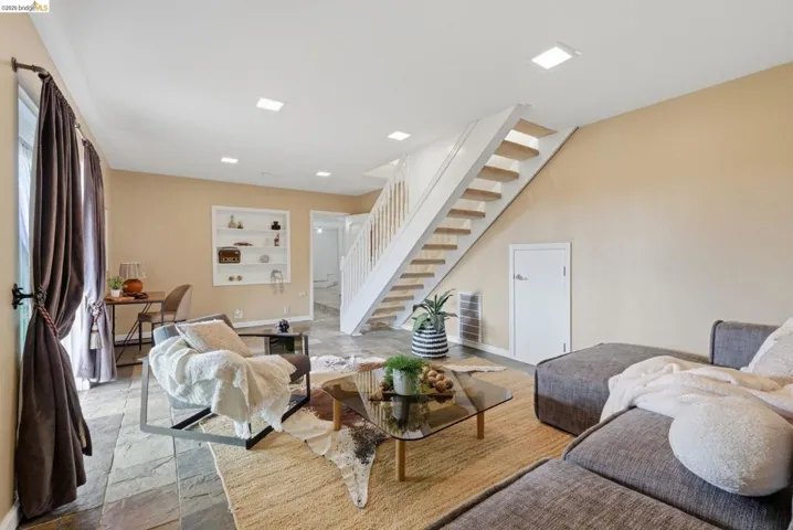 Open concept living area featuring stone tile flooring, a prominent modern staircase with wooden treads, and recessed lighting