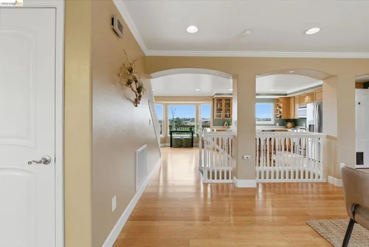 Hallway featuring wood-finish flooring, arched doorways, white trim, recessed lighting, and a partial view of a kitchen with wood cabinetry and stainless steel appliances