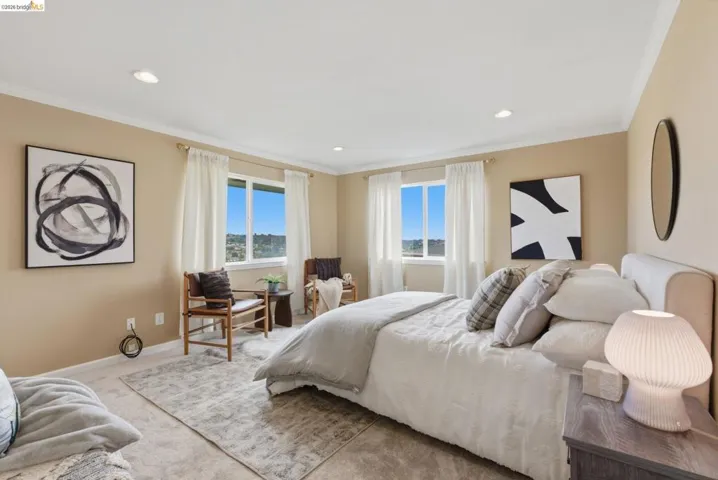 Recessed lighting illuminates this room featuring two large windows with white trim, tan walls, and crown molding