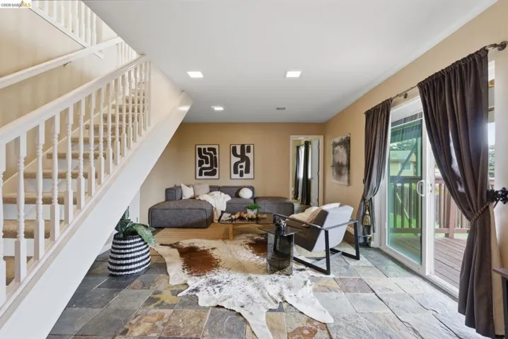 Spacious living area featuring natural slate flooring, a white spindle staircase, and recessed lighting