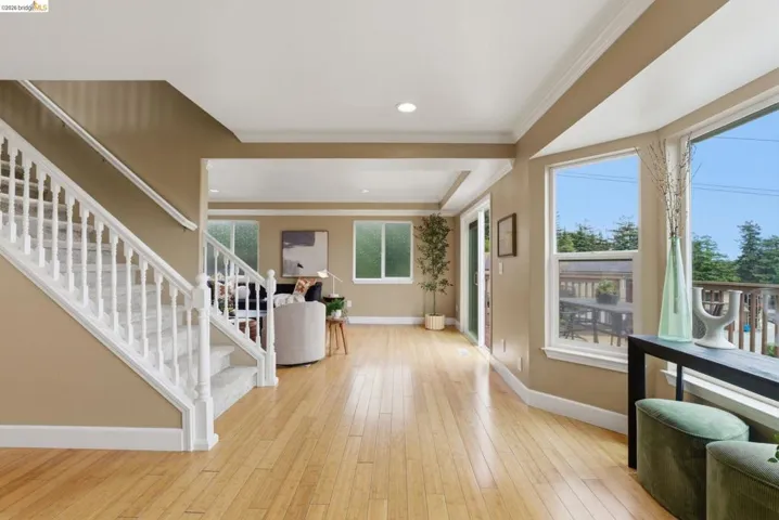 Hardwood-finish flooring extends through an open-concept living area with a white spindle staircase, recessed lighting, and a sliding glass door leading to an exterior deck