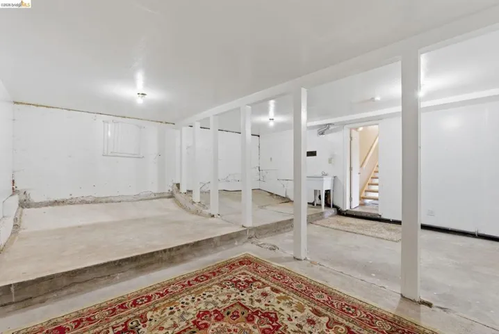 Open lower level featuring exposed support beams, concrete flooring, and a utility sink