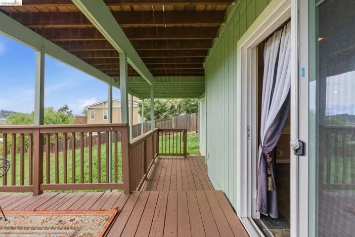 Covered outdoor deck featuring wood-finish flooring, wood railings, and a light green exterior wall