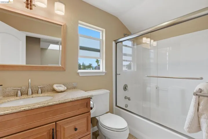 Bathroom featuring a wood-finish vanity with an undermount sink, a light speckled countertop, and brushed nickel fixtures