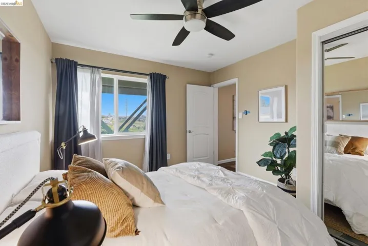 Bedroom featuring a ceiling fan with integrated lighting, large window with outdoor scenery, mirror closet doors, and a paneled interior door