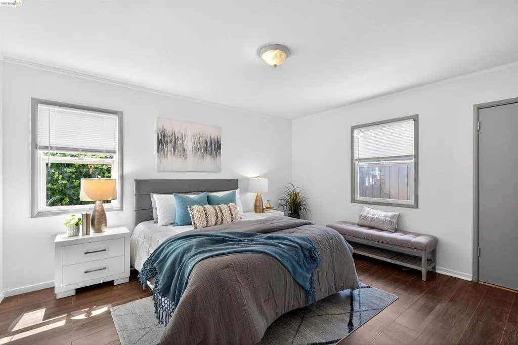 Spacious room featuring wood-finish flooring, two windows with blinds, crown molding, and a flush mount ceiling fixture