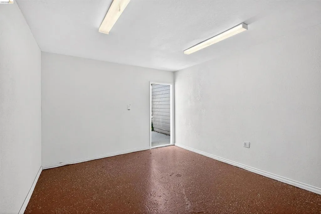 Interior room featuring a durable speckled brown flooring, crisp white walls, and bright overhead fluorescent lighting