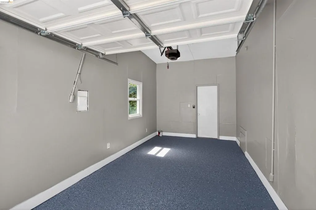 Garage with an epoxy floor, painted walls, a white side access door, a single window, and an automatic garage door opener