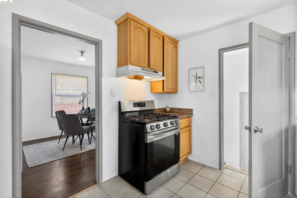 Kitchen featuring light wood cabinetry, stone-finish countertops, and a stainless steel oven/range with an integrated hood