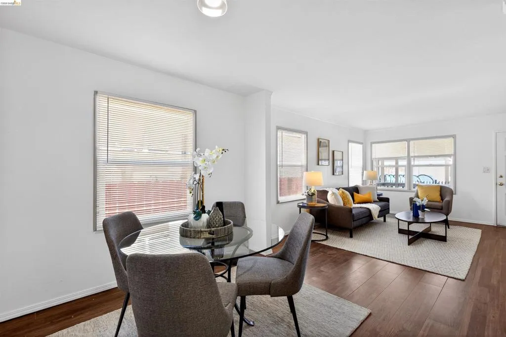 Open-concept living area featuring wood-finish flooring, white walls, and multiple windows with blinds