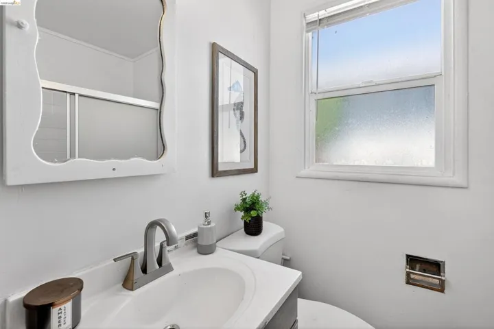 Bathroom featuring a vanity with an integrated sink, a rectangular window with blinds, and a mirror with a decorative frame