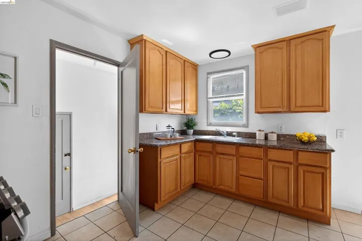 Kitchen featuring wood cabinetry, speckled countertops, a double basin sink with a window, recessed lighting, and tile flooring