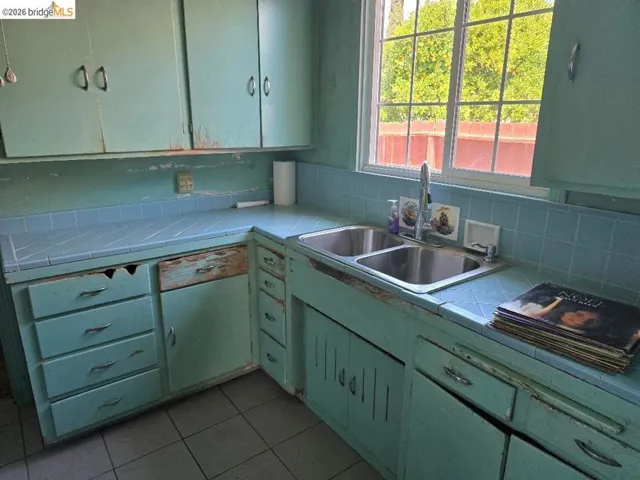 Kitchen featuring a dual-basin stainless steel sink, tiled countertops, and a window with exterior views