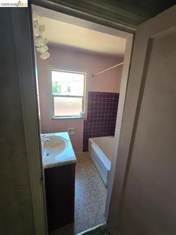 Bathroom featuring a built-in vanity with integrated sink, a bathtub with purple tile surround, and a window for natural illumination