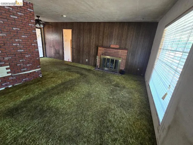 Living area featuring wood-panel walls, green carpeting, and a brick fireplace with a metal insert