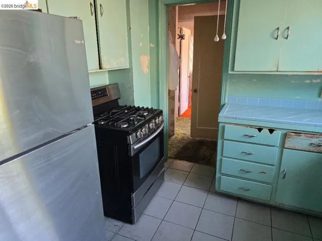 Kitchen featuring a stainless steel refrigerator, black and stainless steel range, and tile flooring