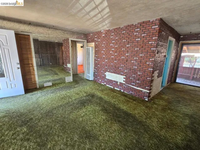 Living area featuring green shag carpeting, brick-patterned wall covering, a mirrored wall, and a white paneled door with decorative glass