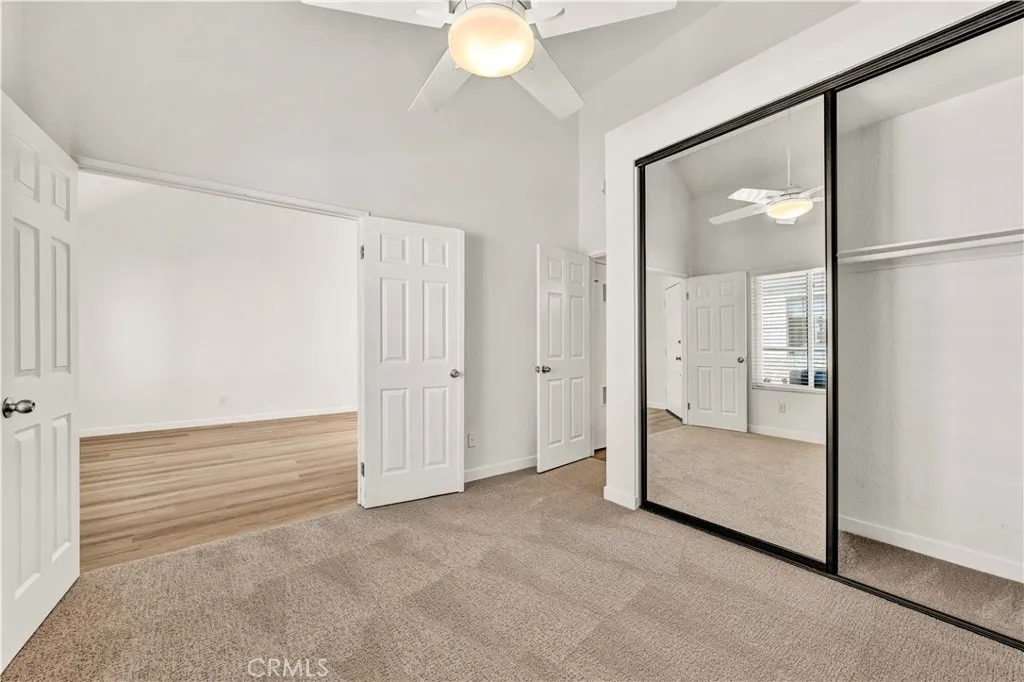 Double door entry into guest bedroom with ceiling fan, mirrored closet, and new carpet