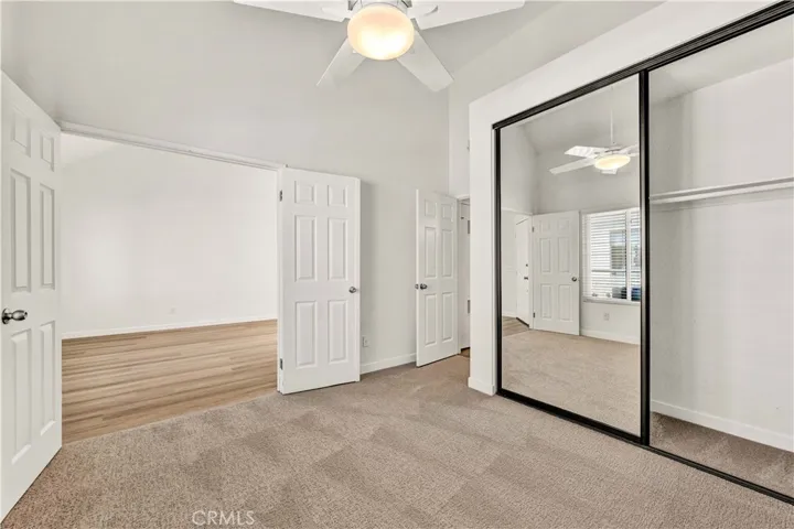 Double door entry into guest bedroom with ceiling fan, mirrored closet, and new carpet