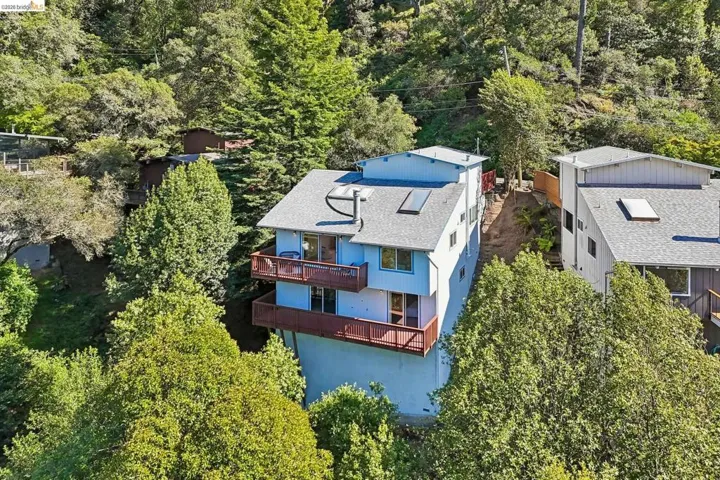Multi-level residence featuring a light blue exterior, two private balconies with wood railings, a gray shingled roof, and multiple skylights