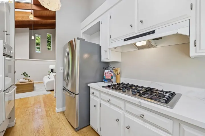 Modern kitchen featuring white cabinetry with silver hardware, an integrated gas cooktop, and a stainless steel refrigerator