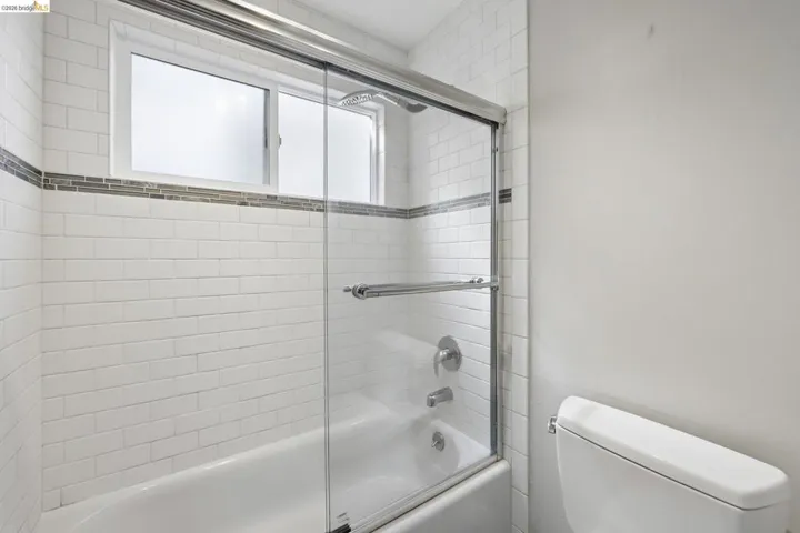 Bathtub and shower combination featuring white subway tile, a decorative glass tile accent band, and a sliding glass enclosure