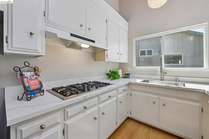 Kitchen featuring white cabinetry, light-toned countertops, an undermount stainless steel sink with a gooseneck faucet, a built-in gas cooktop, and wood-finish flooring