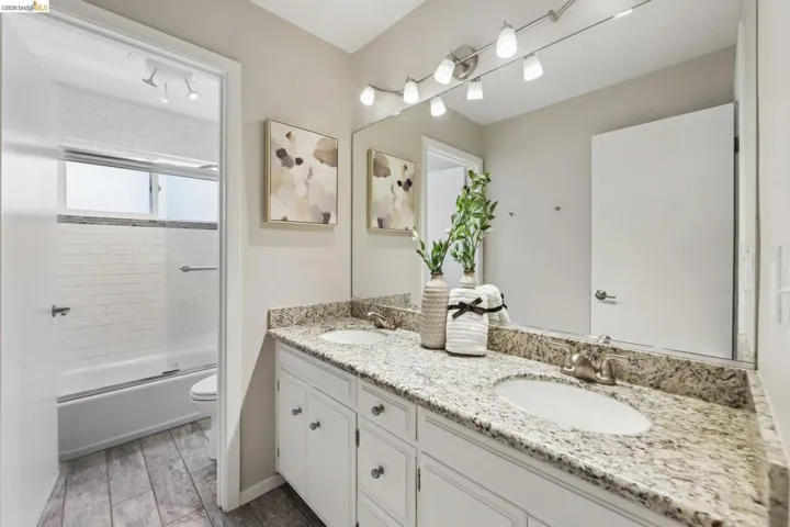 Bathroom featuring a dual-sink vanity with a speckled countertop, white cabinetry, and brushed nickel hardware