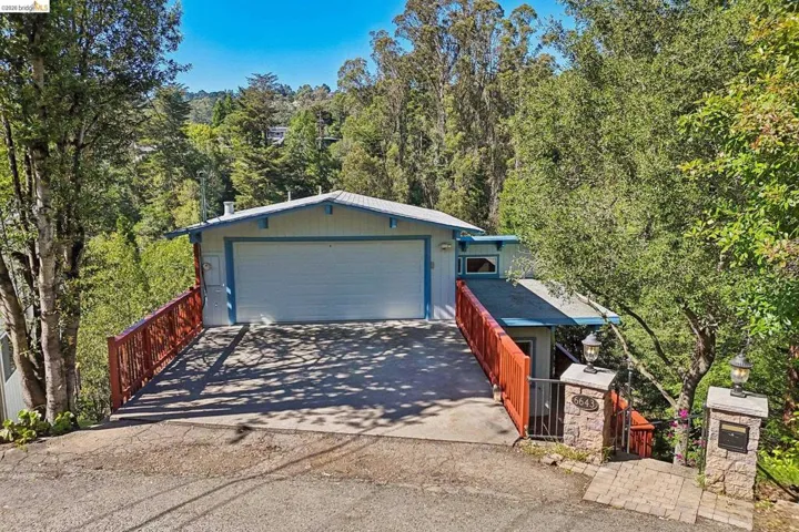 Single-story residence featuring an integrated garage, a concrete driveway, and a red-toned wooden railing system