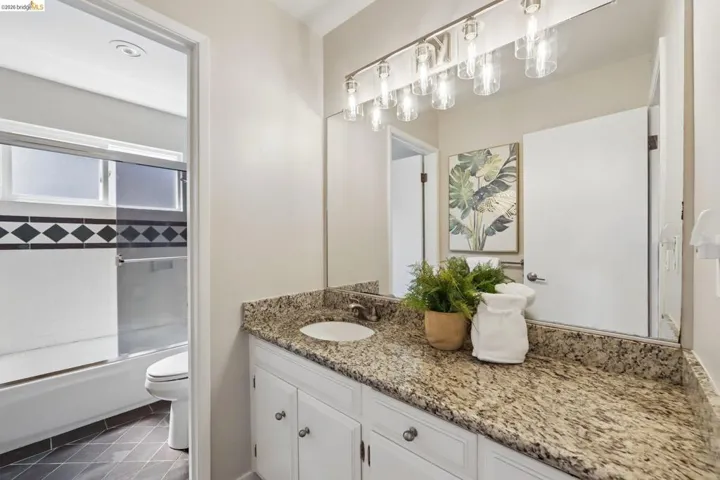 Bathroom vanity featuring a granite-style countertop, undermount sink, and white cabinetry with brushed nickel hardware