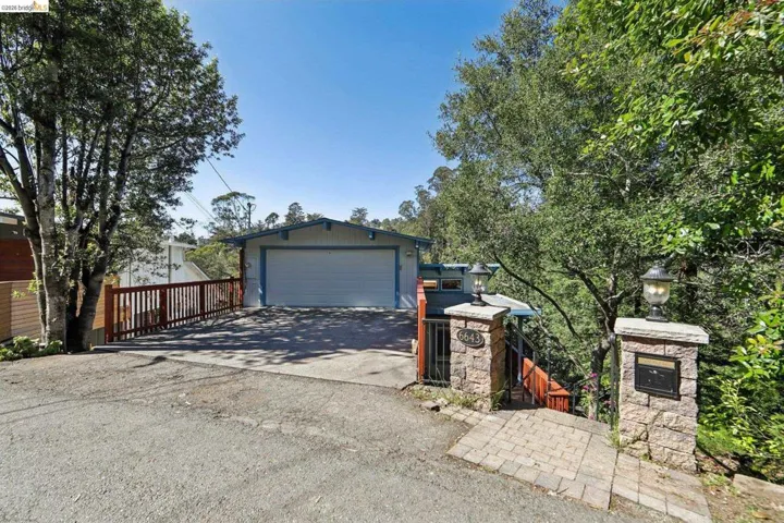 Front exterior featuring an attached garage, paved driveway, and stone entry pillars with integrated lighting and mailbox
