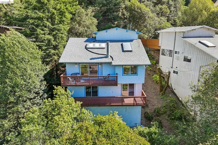 Multi-level residence featuring a light blue exterior, dual balconies with wood railings, and a gray shingle roof with skylights