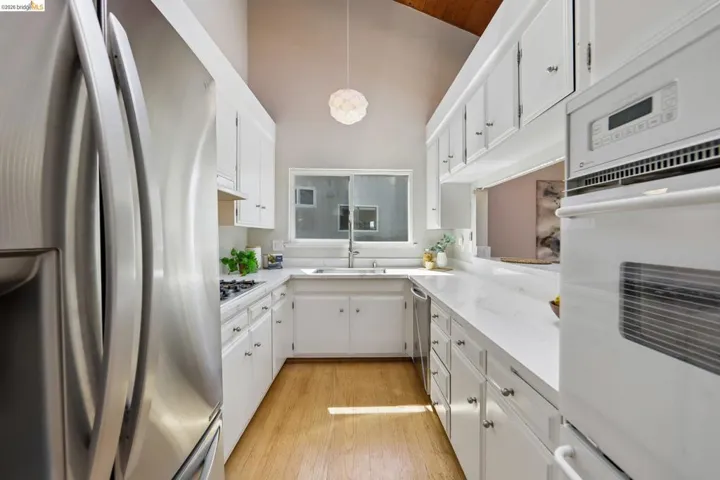 Contemporary kitchen featuring a vaulted wood-finish ceiling, white cabinetry, integrated oven, stainless steel refrigerator, and wood-finish flooring