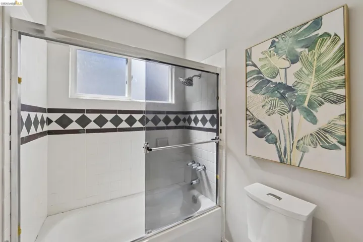 Bathroom featuring a shower-tub combination with sliding glass doors, white subway tile walls, a decorative black and white diamond-patterned accent tile, and an opaque window