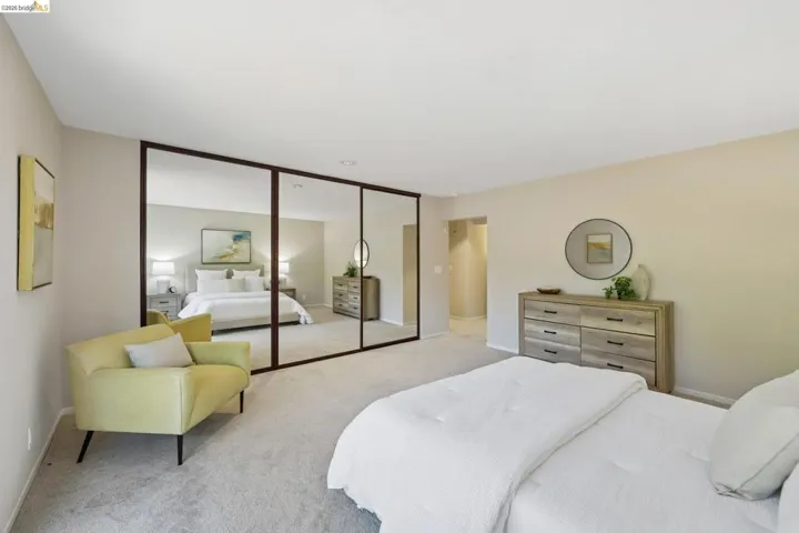 Expansive bedroom featuring wall-to-wall mirrored closet doors, neutral carpeting, and light-toned wall finishes