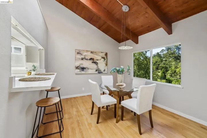 Dining area featuring a vaulted wood-beam ceiling, light wood-finish flooring, and a pass-through window with a breakfast bar